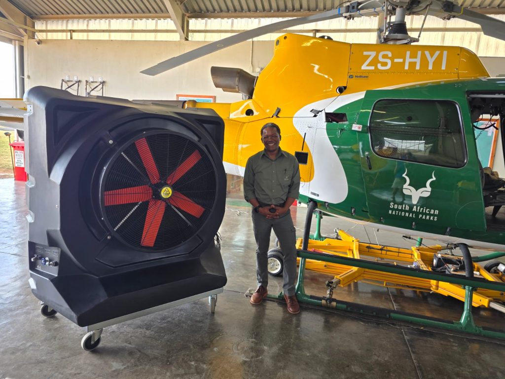 Mr Simelane from SANParks Skukuza Airport standing beside a MaxCool industrial evaporative cooler in the helicopter hangar to improve working conditions and reduce heat stress.